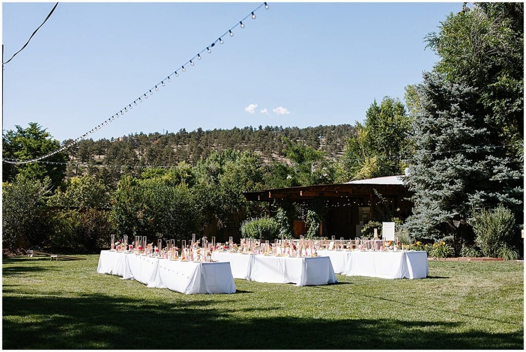 Long tables set up with white linens for wedding reception on the lawn